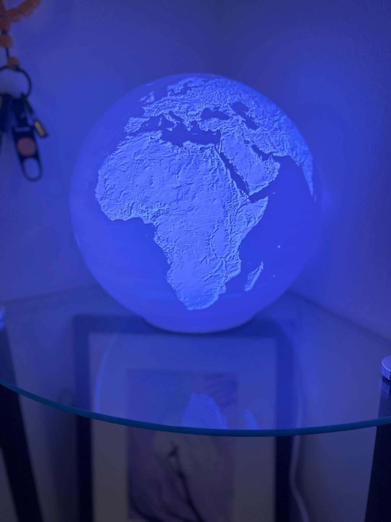 A 3D-printed globe lamp showing Earth's topography, featuring color-changing LED lights that transition from white to blue.