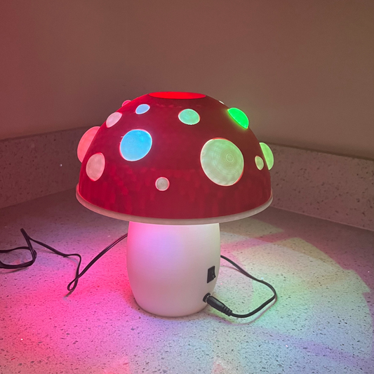 A 3D-printed mushroom lamp with a vibrant red cap and glowing colorful spots, casting a warm light on a countertop.